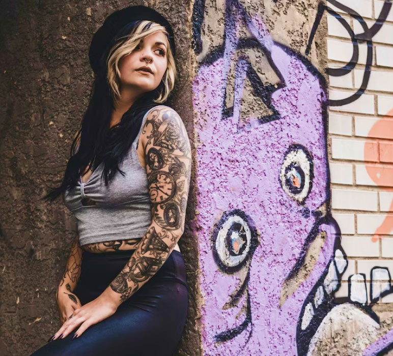Woman with Tattooed Arms Standing Against Graffiti Wall Woman with Tattooed Arms Standing Against Graffiti Wall